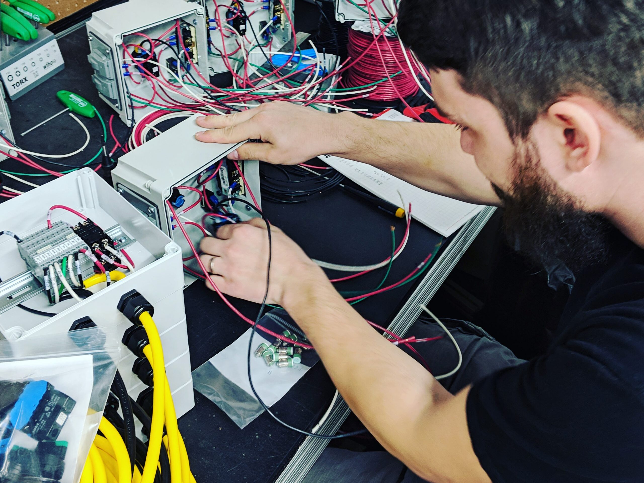 Employee works on an electrical control panel with red and yellow wires.